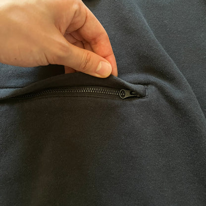 Adidas Trefoil Zip Pouch Hoodie in black, crafted from soft cotton for durability and comfort. Features a large Trefoil logo on the back within a circle, a smaller embroidered logo on the left chest, and a front zip pouch pocket. Designed with thick drawstrings and reinforced stitching, offering a sturdy, well-constructed fit.