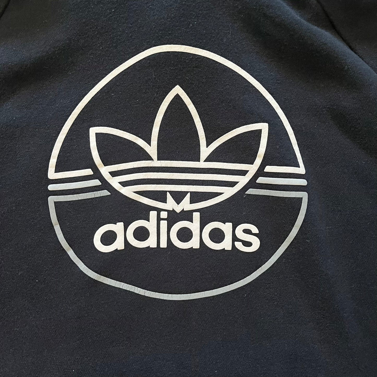 Adidas Trefoil Zip Pouch Hoodie in black, crafted from soft cotton for durability and comfort. Features a large Trefoil logo on the back within a circle, a smaller embroidered logo on the left chest, and a front zip pouch pocket. Designed with thick drawstrings and reinforced stitching, offering a sturdy, well-constructed fit.