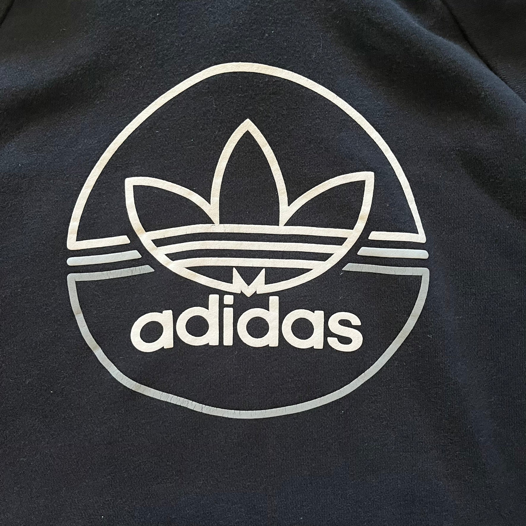 Adidas Trefoil Zip Pouch Hoodie in black, crafted from soft cotton for durability and comfort. Features a large Trefoil logo on the back within a circle, a smaller embroidered logo on the left chest, and a front zip pouch pocket. Designed with thick drawstrings and reinforced stitching, offering a sturdy, well-constructed fit.