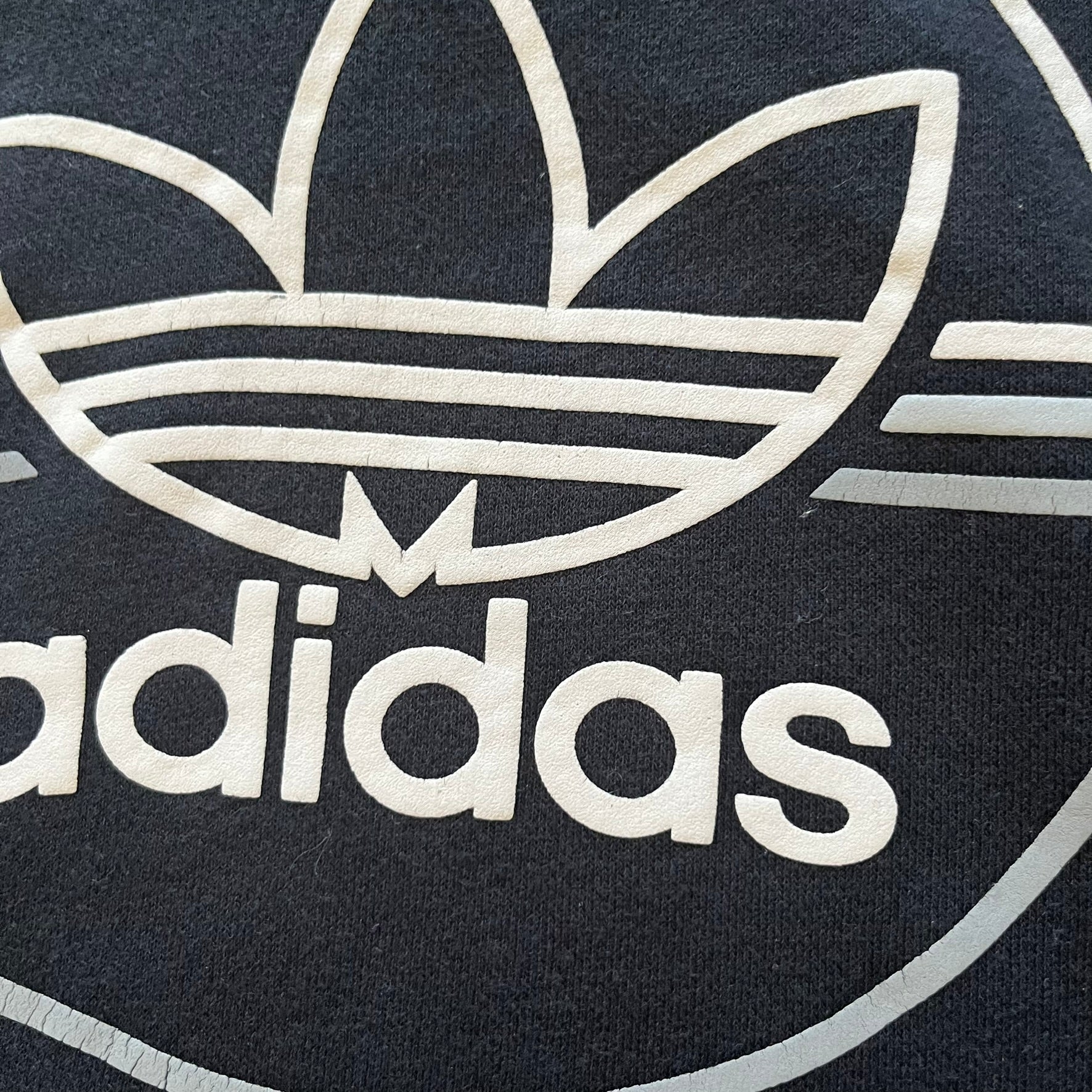 Adidas Trefoil Zip Pouch Hoodie in black, crafted from soft cotton for durability and comfort. Features a large Trefoil logo on the back within a circle, a smaller embroidered logo on the left chest, and a front zip pouch pocket. Designed with thick drawstrings and reinforced stitching, offering a sturdy, well-constructed fit.