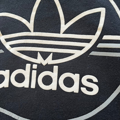 Adidas Trefoil Zip Pouch Hoodie in black, crafted from soft cotton for durability and comfort. Features a large Trefoil logo on the back within a circle, a smaller embroidered logo on the left chest, and a front zip pouch pocket. Designed with thick drawstrings and reinforced stitching, offering a sturdy, well-constructed fit.