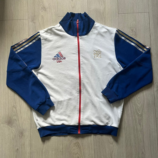 Adidas USA Olympic London 2012 Track Jacket in white with a blue sleeve featuring bronze, silver, and gold adidas stripes. Designed with a red zipper, blue collar, and embroidered adidas USA logo in a flag graphic on the chest, paired with a gold embroidered London 2012 logo on the other side. A rare piece of official Team USA gear from the London Olympic Games.