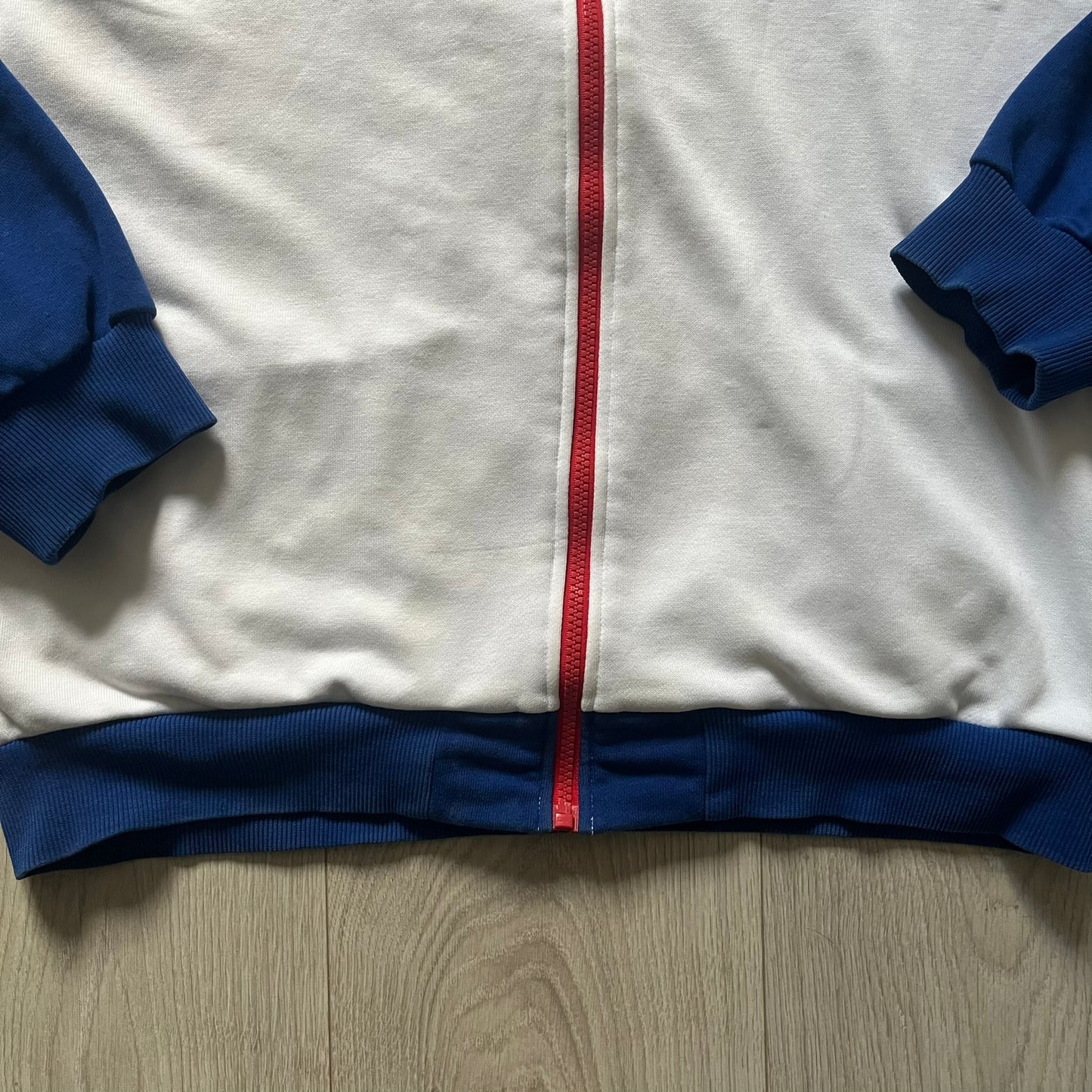 Adidas USA Olympic London 2012 Track Jacket in white with a blue sleeve featuring bronze, silver, and gold adidas stripes. Designed with a red zipper, blue collar, and embroidered adidas USA logo in a flag graphic on the chest, paired with a gold embroidered London 2012 logo on the other side. A rare piece of official Team USA gear from the London Olympic Games.