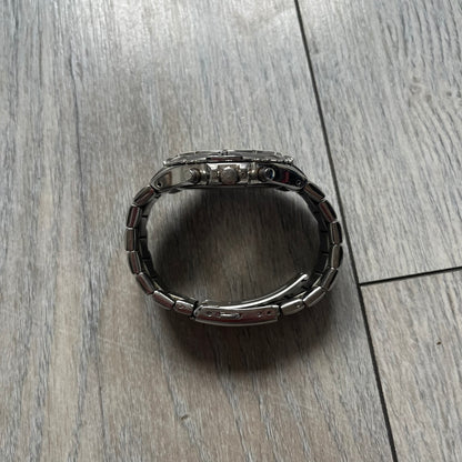 Adidas VS Chronograph 10-5010 Analog Watch is a silver-tone metal timepiece featuring a metallic blue dial with day and seconds indicators. The watch includes three sub-dials, a detailed seconds track, and three side buttons for chronograph functions. Designed with a sturdy, thick case, it comes with an extra link for adjustable sizing.