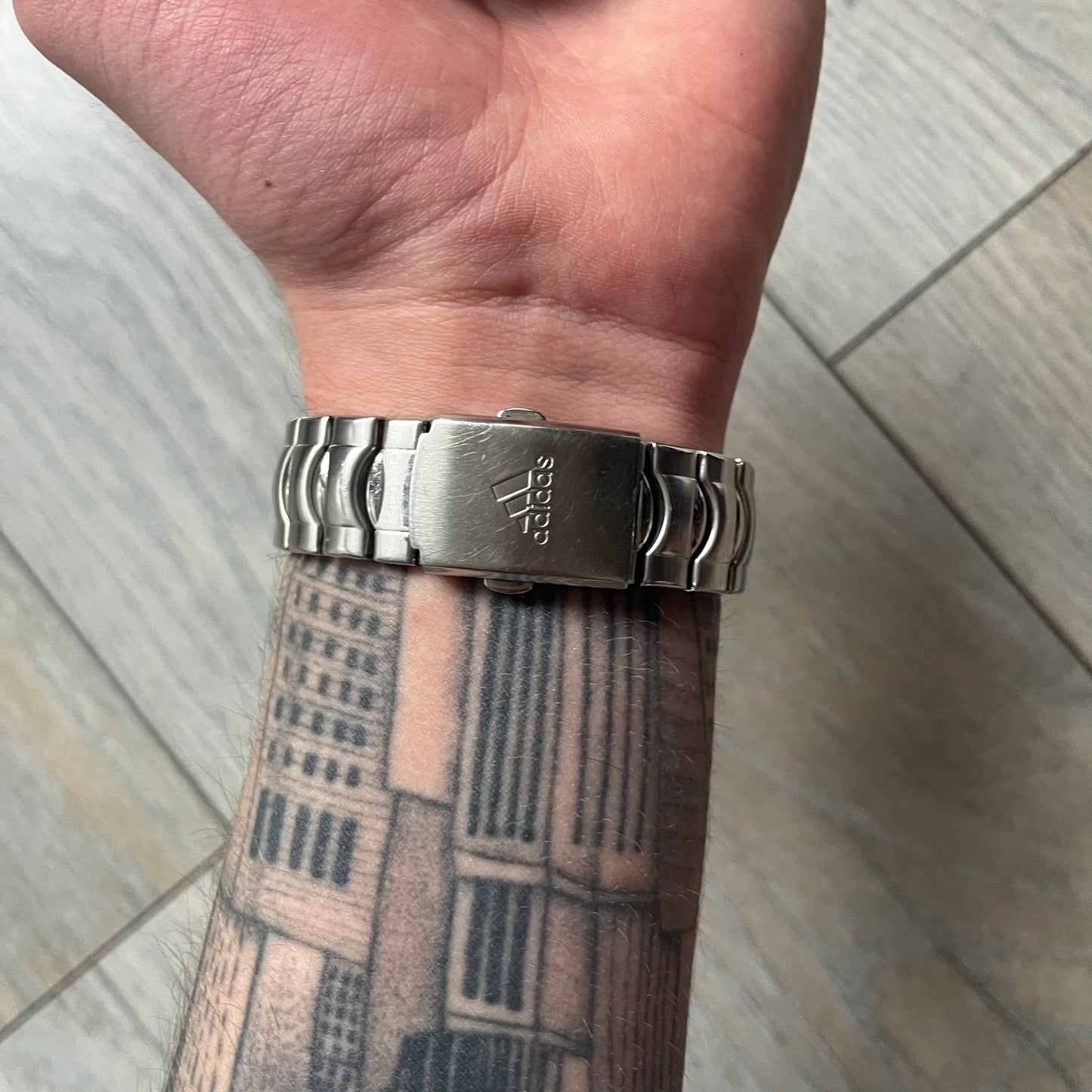 Adidas VS Chronograph 10-5010 Analog Watch is a silver-tone metal timepiece featuring a metallic blue dial with day and seconds indicators. The watch includes three sub-dials, a detailed seconds track, and three side buttons for chronograph functions. Designed with a sturdy, thick case, it comes with an extra link for adjustable sizing.