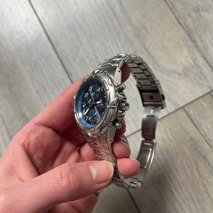 Adidas VS Chronograph 10-5010 Analog Watch is a silver-tone metal timepiece featuring a metallic blue dial with day and seconds indicators. The watch includes three sub-dials, a detailed seconds track, and three side buttons for chronograph functions. Designed with a sturdy, thick case, it comes with an extra link for adjustable sizing.