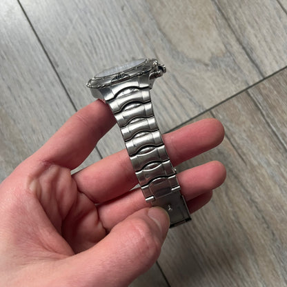 Adidas VS Chronograph 10-5010 Analog Watch is a silver-tone metal timepiece featuring a metallic blue dial with day and seconds indicators. The watch includes three sub-dials, a detailed seconds track, and three side buttons for chronograph functions. Designed with a sturdy, thick case, it comes with an extra link for adjustable sizing.