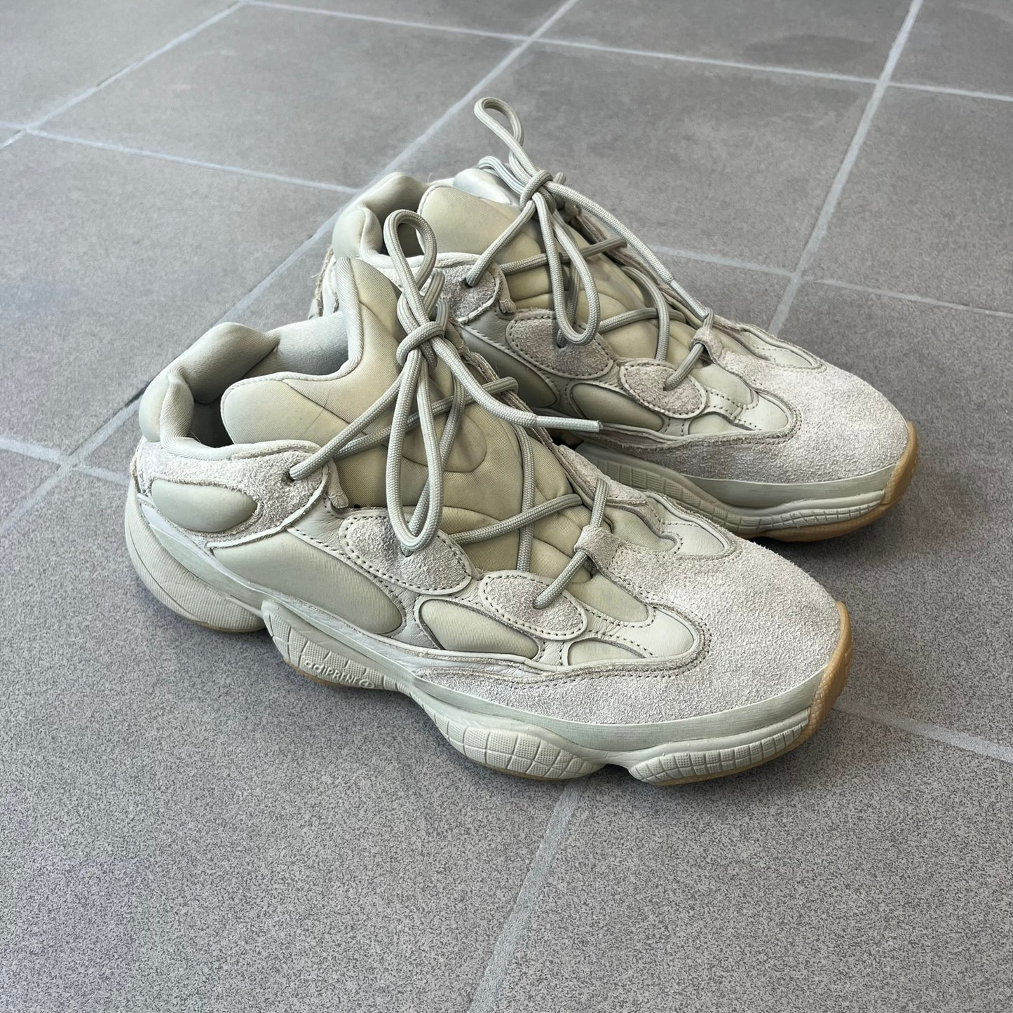 Adidas Yeezy 500 “Stone” Sneakers feature a Stone/Stone/Stone colorway with suede and neoprene paneling, reflective piping, and a pull-tab at the tongue. The sneakers have a lace-up fastening, adiPRENE midsole, and gum rubber outsole. Style FW4839, released November 23, 2019.
