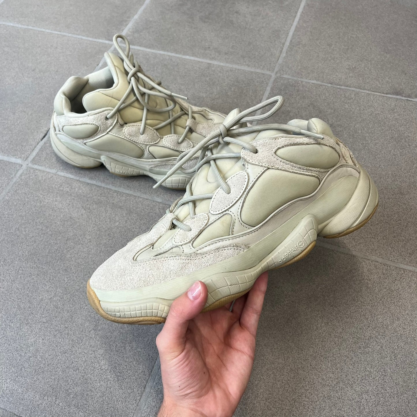 Adidas Yeezy 500 “Stone” Sneakers feature a Stone/Stone/Stone colorway with suede and neoprene paneling, reflective piping, and a pull-tab at the tongue. The sneakers have a lace-up fastening, adiPRENE midsole, and gum rubber outsole. Style FW4839, released November 23, 2019.

