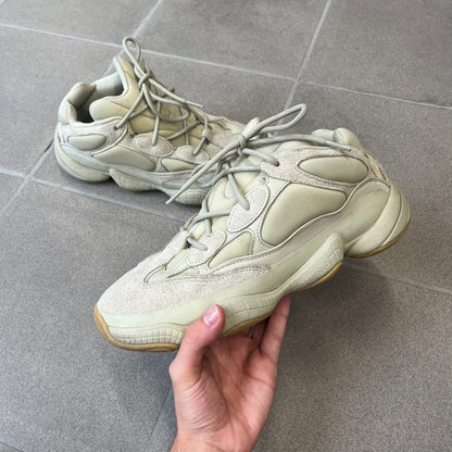Adidas Yeezy 500 “Stone” Sneakers feature a Stone/Stone/Stone colorway with suede and neoprene paneling, reflective piping, and a pull-tab at the tongue. The sneakers have a lace-up fastening, adiPRENE midsole, and gum rubber outsole. Style FW4839, released November 23, 2019.
