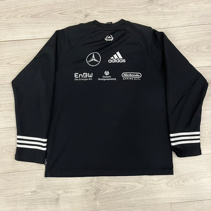 Adidas 2004/05 Germany Longsleeve in black featuring the Talent Förderung logo on the front and a center Adidas chest logo. Designed with classic three white stripes along the wrists and multiple sponsor logos on the back, including Mercedes, Adidas, and Nintendo. Made with Climawear fabric for comfort and performance.