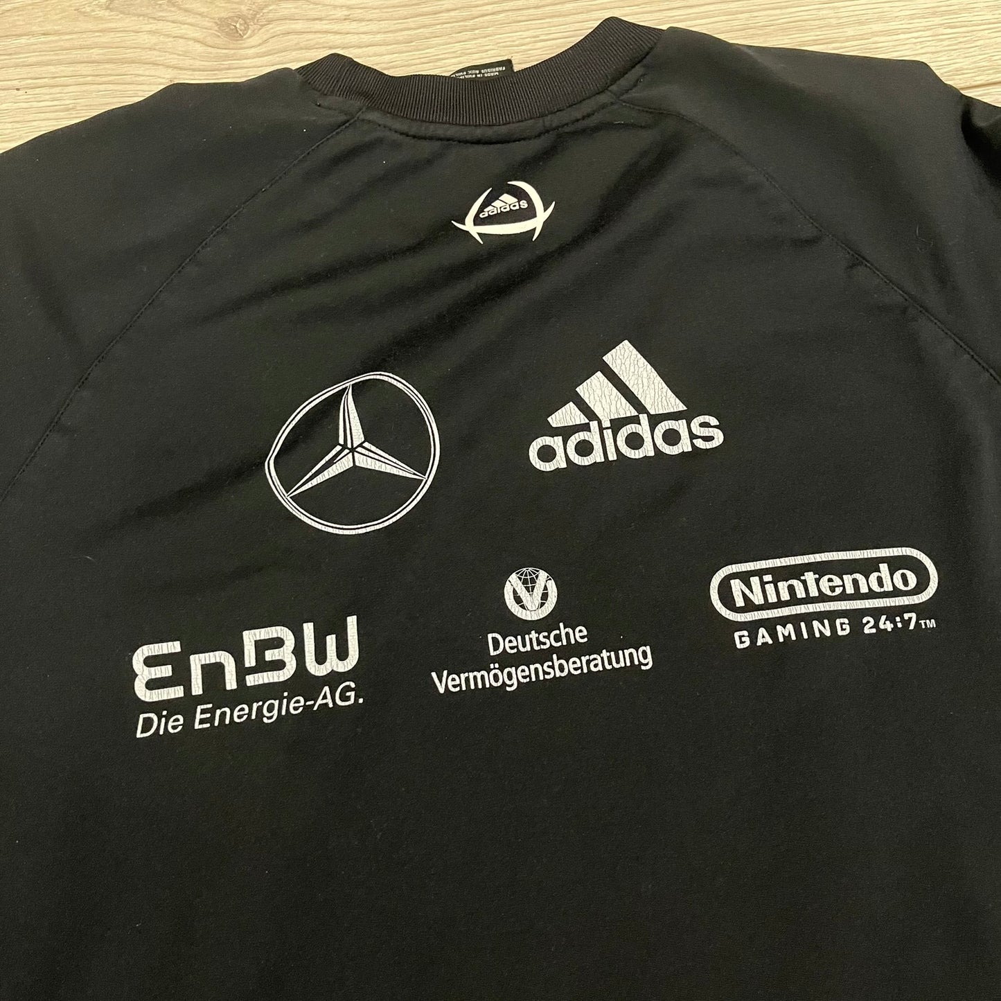 Adidas 2004/05 Germany Longsleeve in black featuring the Talent Förderung logo on the front and a center Adidas chest logo. Designed with classic three white stripes along the wrists and multiple sponsor logos on the back, including Mercedes, Adidas, and Nintendo. Made with Climawear fabric for comfort and performance.