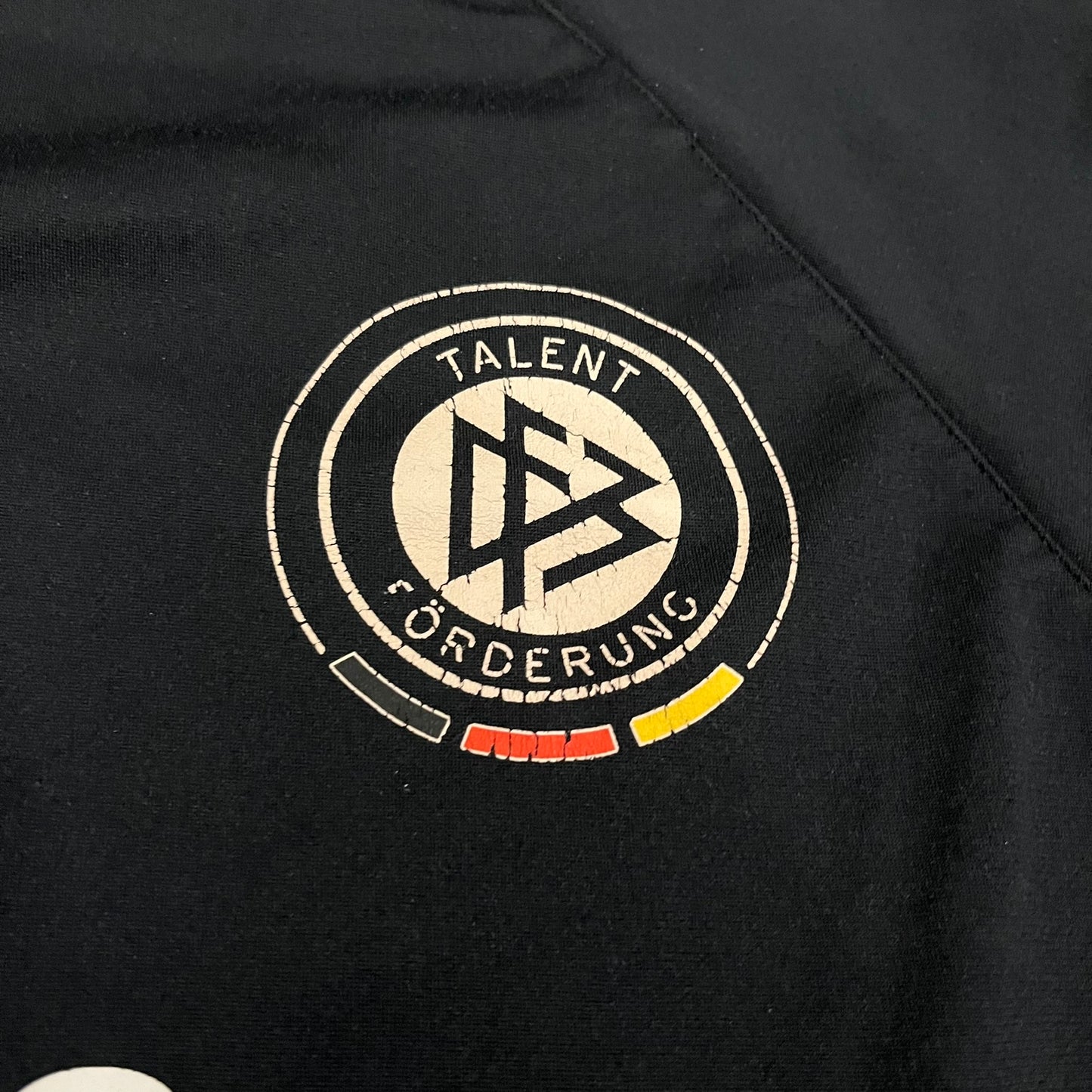 Adidas 2004/05 Germany Longsleeve in black featuring the Talent Förderung logo on the front and a center Adidas chest logo. Designed with classic three white stripes along the wrists and multiple sponsor logos on the back, including Mercedes, Adidas, and Nintendo. Made with Climawear fabric for comfort and performance.