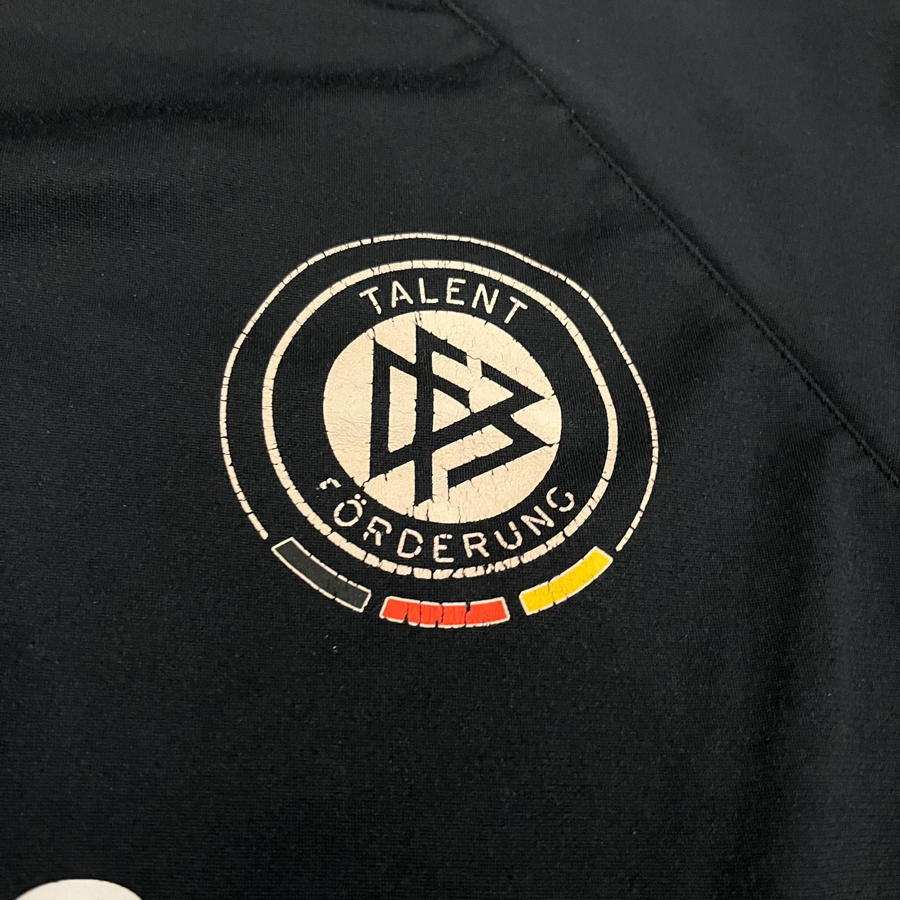 Adidas 2004/05 Germany Longsleeve in black featuring the Talent Förderung logo on the front and a center Adidas chest logo. Designed with classic three white stripes along the wrists and multiple sponsor logos on the back, including Mercedes, Adidas, and Nintendo. Made with Climawear fabric for comfort and performance.