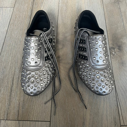 Adidas x Jeremy Scott 2010 Sample “Rockstar” Shoes (Article G16255) are a rare sample pair from the Spring/Summer 2010 collection, produced in June 2009. The shoes feature a metallic leather upper fully covered in circular rhinestone studs, with black Adidas three-stripe detailing on the sides and white soles. This model is built on a slim taekwondo-style silhouette and includes a yellow sample tag card.