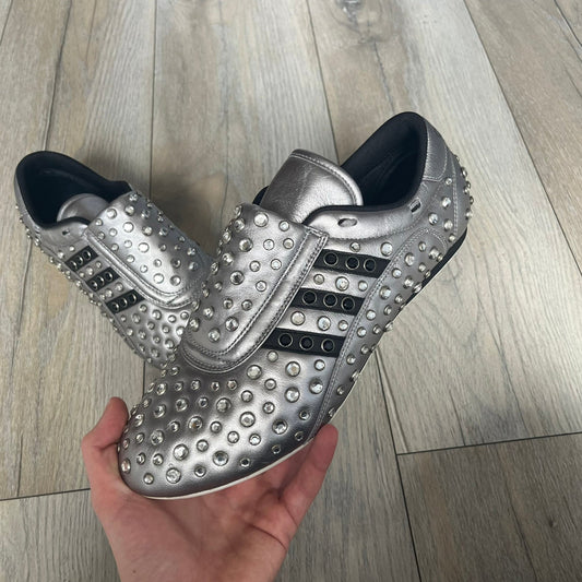 Adidas x Jeremy Scott 2010 Sample “Rockstar” Shoes (Article G16255) are a rare sample pair from the Spring/Summer 2010 collection, produced in June 2009. The shoes feature a metallic leather upper fully covered in circular rhinestone studs, with black Adidas three-stripe detailing on the sides and white soles. This model is built on a slim taekwondo-style silhouette and includes a yellow sample tag card.
