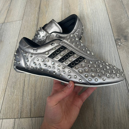 Adidas x Jeremy Scott 2010 Sample “Rockstar” Shoes (Article G16255) are a rare sample pair from the Spring/Summer 2010 collection, produced in June 2009. The shoes feature a metallic leather upper fully covered in circular rhinestone studs, with black Adidas three-stripe detailing on the sides and white soles. This model is built on a slim taekwondo-style silhouette and includes a yellow sample tag card.