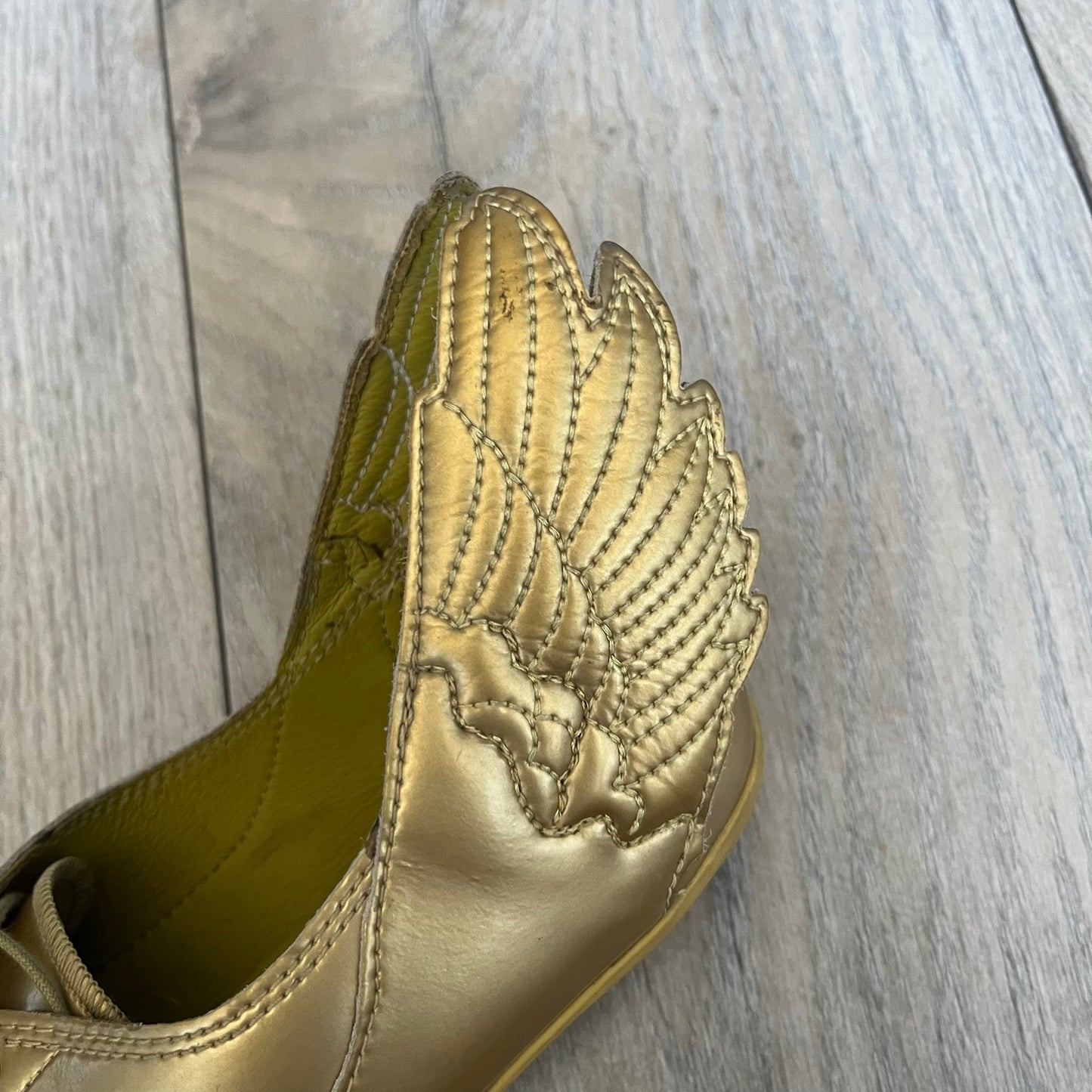 Adidas x Jeremy Scott 2011 Wings Gold Ballet Flats are a rare footwear design combining a classic ballet flat silhouette with Jeremy Scott’s signature wing motif. The shoes feature a fully metallic gold finish with visible stitching throughout the upper and wing construction. Small 3D wings extend from both sides of the heel area, creating the iconic Wings look in a streamlined form. Finished with a Trefoil Adidas logo on the back.