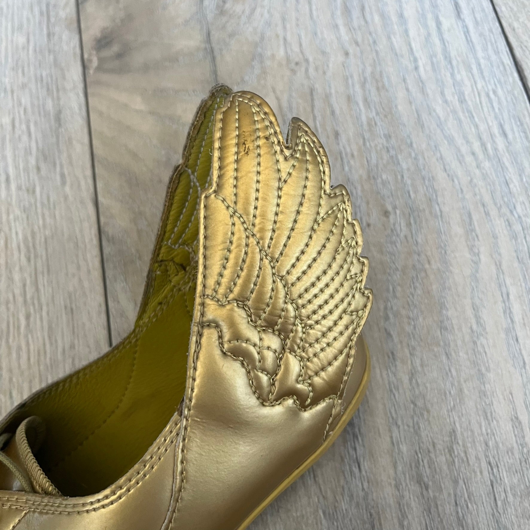 Adidas x Jeremy Scott 2011 Wings Gold Ballet Flats are a rare footwear design combining a classic ballet flat silhouette with Jeremy Scott’s signature wing motif. The shoes feature a fully metallic gold finish with visible stitching throughout the upper and wing construction. Small 3D wings extend from both sides of the heel area, creating the iconic Wings look in a streamlined form. Finished with a Trefoil Adidas logo on the back.