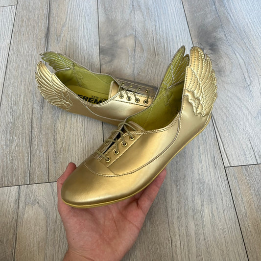 Adidas x Jeremy Scott 2011 Wings Gold Ballet Flats are a rare footwear design combining a classic ballet flat silhouette with Jeremy Scott’s signature wing motif. The shoes feature a fully metallic gold finish with visible stitching throughout the upper and wing construction. Small 3D wings extend from both sides of the heel area, creating the iconic Wings look in a streamlined form. Finished with a Trefoil Adidas logo on the back.