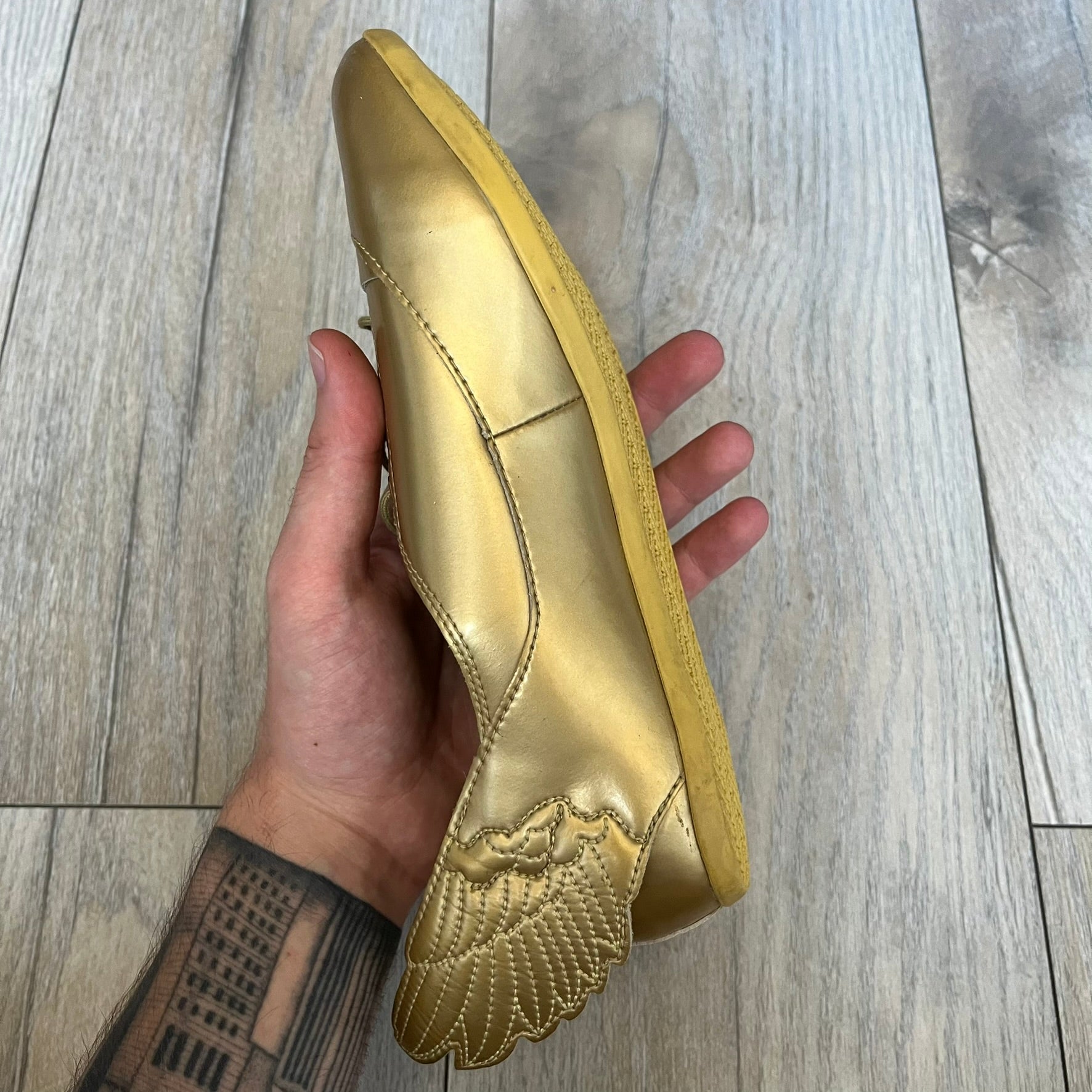 Adidas x Jeremy Scott 2011 Wings Gold Ballet Flats are a rare footwear design combining a classic ballet flat silhouette with Jeremy Scott’s signature wing motif. The shoes feature a fully metallic gold finish with visible stitching throughout the upper and wing construction. Small 3D wings extend from both sides of the heel area, creating the iconic Wings look in a streamlined form. Finished with a Trefoil Adidas logo on the back.