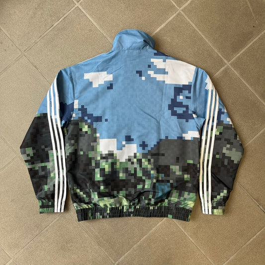 Adidas x Minecraft Movie SS25 Track Top (Style: JZ9921) is a Spring/Summer 2025 collaboration featuring an all-over Minecraft landscape print with a pixelated sky across the upper half and grass terrain across the lower half. The track jacket has white Three Stripes along the shoulders and sleeves, a full-zip front with a pixelated Trefoil logo zipper pull, and ribbed cuffs and hem. Finished in Hazy Blue, Magic Lime, and Tribe Green.