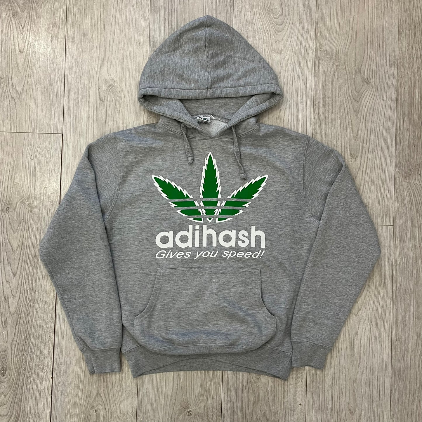 This Adihash “Gives You Speed!” Hoodie features a playful twist on the classic adidas emblem, replacing the trefoil with three marijuana leaves and big Adihash branding. Made from a soft polyester–cotton blend, it offers everyday comfort with a standard pouch pocket and a clean grey finish. Produced on a Lemon Collection blank.