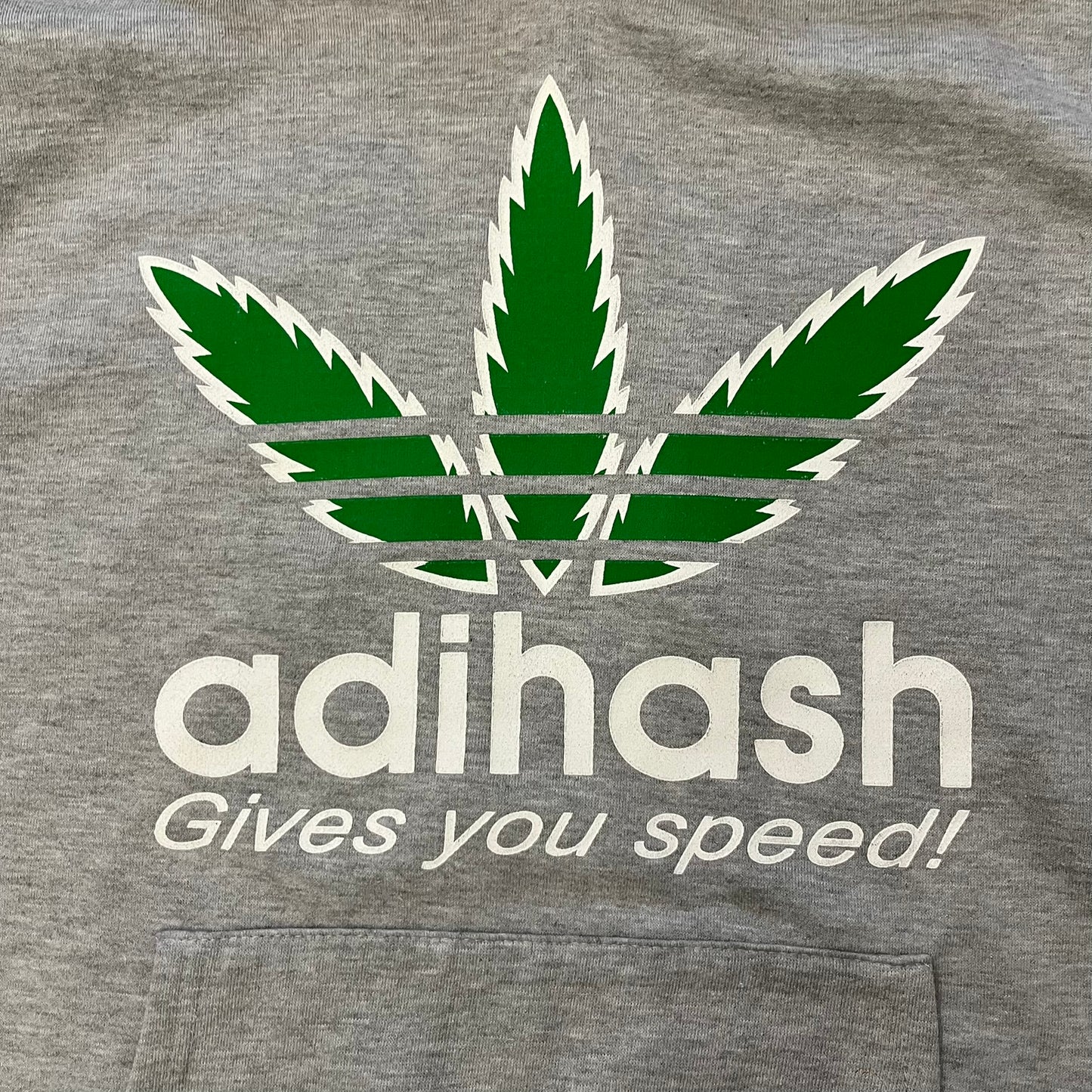 This Adihash “Gives You Speed!” Hoodie features a playful twist on the classic adidas emblem, replacing the trefoil with three marijuana leaves and big Adihash branding. Made from a soft polyester–cotton blend, it offers everyday comfort with a standard pouch pocket and a clean grey finish. Produced on a Lemon Collection blank.