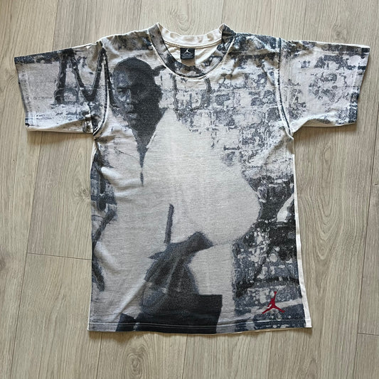 Air Jordan 2000’s All Over Print Tee featuring a bold full print of Michael Jordan in black, white, and blue across the front. A small red Jumpman logo sits at the bottom, while the back showcases a large Air Jordan logo with embroidered small red logo just under the collar. A rare vintage piece from the 2000s that captures peak Jordan era style.