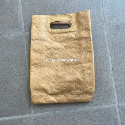 Alexander Wang x McDonald’s 2019 Golden Lunch Bag is a limited edition collaboration accessory made from thick waterproof DuPont Tyvek paper with a leather-like texture. Designed to resemble a classic McDonald’s takeaway bag, it features a small white Alexander Wang logo on the front and a subtle McDonald’s Golden Arches logo on the side. The piece combines fast-food nostalgia with Alexander Wang’s minimalist luxury approach.
