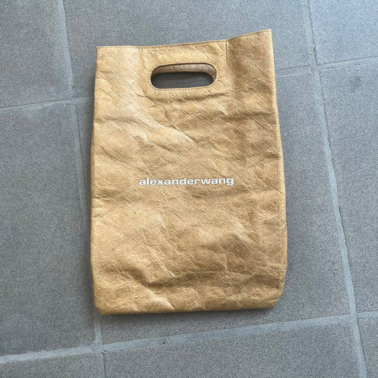 Alexander Wang x McDonald’s 2019 Golden Lunch Bag is a limited edition collaboration accessory made from thick waterproof DuPont Tyvek paper with a leather-like texture. Designed to resemble a classic McDonald’s takeaway bag, it features a small white Alexander Wang logo on the front and a subtle McDonald’s Golden Arches logo on the side. The piece combines fast-food nostalgia with Alexander Wang’s minimalist luxury approach.
