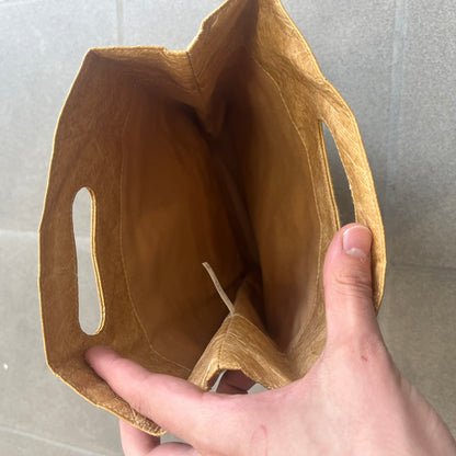 Alexander Wang x McDonald’s 2019 Golden Lunch Bag is a limited edition collaboration accessory made from thick waterproof DuPont Tyvek paper with a leather-like texture. Designed to resemble a classic McDonald’s takeaway bag, it features a small white Alexander Wang logo on the front and a subtle McDonald’s Golden Arches logo on the side. The piece combines fast-food nostalgia with Alexander Wang’s minimalist luxury approach.

