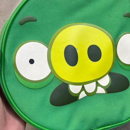 Angry Birds 2010s Bad Piggies Green Backpack is a small circular backpack shaped like the head of a Bad Piggies character. The front features the pig’s scared facial expression, while the side has an Angry Birds logo. The interior includes an all-over pig head monogram lining and an official Angry Birds licensed tag. The backpack is finished with really short adjustable shoulder straps.