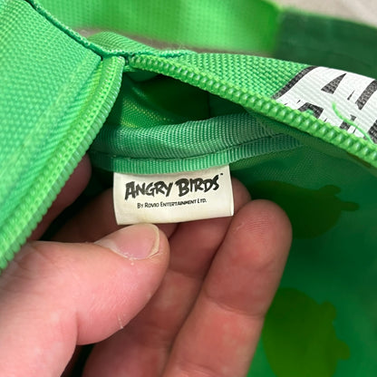 Angry Birds 2010s Bad Piggies Green Backpack is a small circular backpack shaped like the head of a Bad Piggies character. The front features the pig’s scared facial expression, while the side has an Angry Birds logo. The interior includes an all-over pig head monogram lining and an official Angry Birds licensed tag. The backpack is finished with really short adjustable shoulder straps.