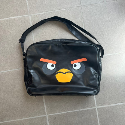 Angry Birds 2010s Black Bomb Bird Shoulder Bag is a black messenger-style bag made from a leather-like material. It features one main compartment with a smaller internal pocket. The front is designed with a large graphic of Bomb, the black Angry Birds character. The interior includes official Angry Birds 2009-2013 licensing.