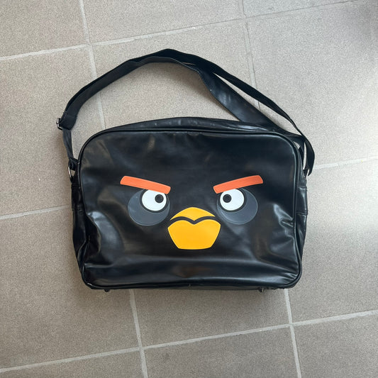 Angry Birds 2010s Black Bomb Bird Shoulder Bag is a black messenger-style bag made from a leather-like material. It features one main compartment with a smaller internal pocket. The front is designed with a large graphic of Bomb, the black Angry Birds character. The interior includes official Angry Birds 2009-2013 licensing.