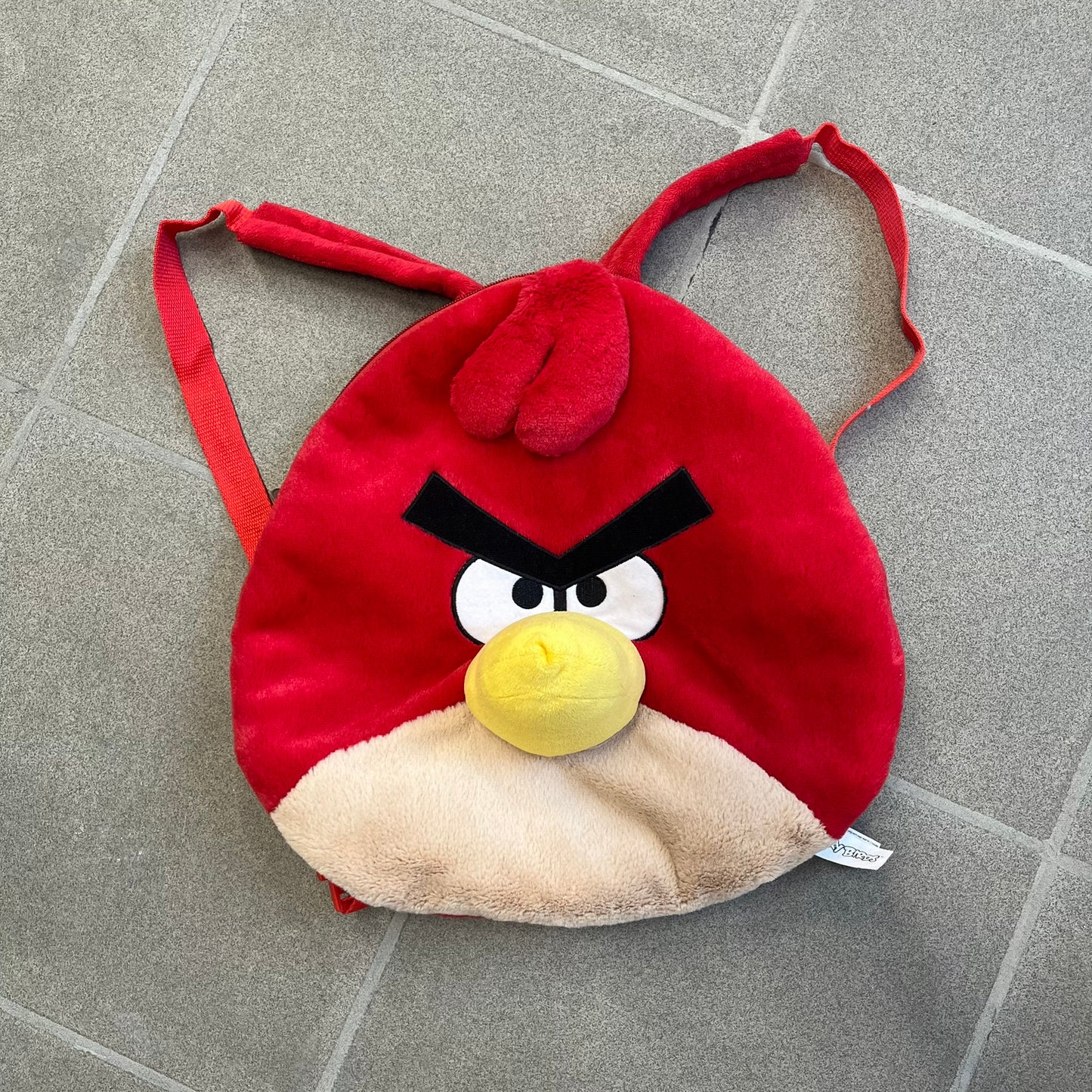 Angry Birds 2010s Red Bird Backpack is a small backpack shaped like Red, the iconic Angry Birds character. It features an angry facial expression with a three-dimensional beak and feather details, along with adjustable red shoulder straps. The interior includes official Angry Birds 2011 licensing.
