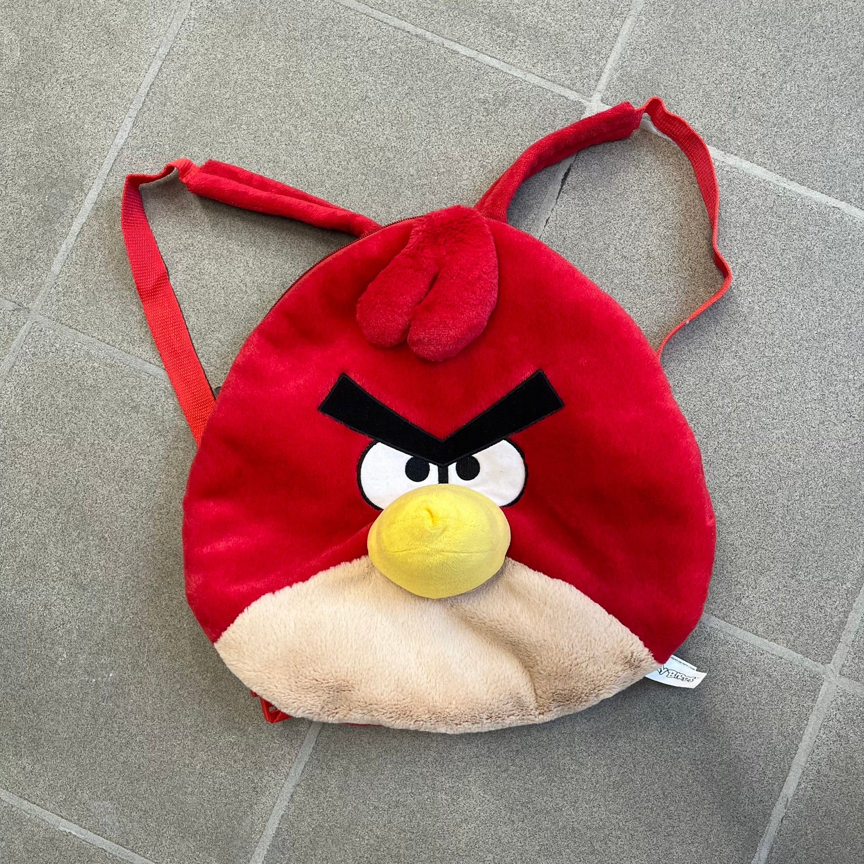 Angry Birds 2010s Red Bird Backpack is a small backpack shaped like Red, the iconic Angry Birds character. It features an angry facial expression with a three-dimensional beak and feather details, along with adjustable red shoulder straps. The interior includes official Angry Birds 2011 licensing.

