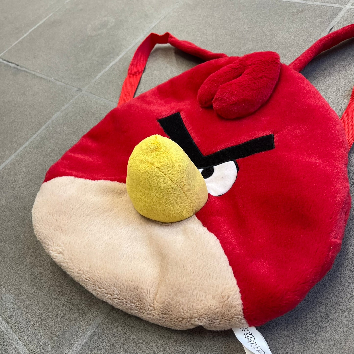 Angry Birds 2010s Red Bird Backpack is a small backpack shaped like Red, the iconic Angry Birds character. It features an angry facial expression with a three-dimensional beak and feather details, along with adjustable red shoulder straps. The interior includes official Angry Birds 2011 licensing.
