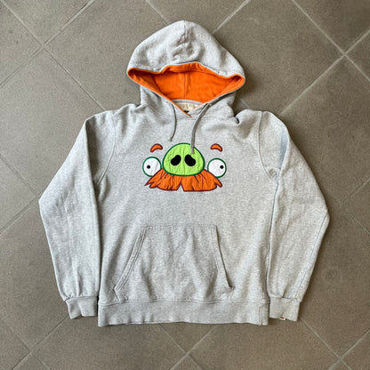 Angry Birds Three Star 2012 Foreman Pig Gray Hoodie features a grey hoodie design with a 3D-style front graphic of Foreman Pig, showing his recognizable eyes, nose, and mustache details. The back features a grey circular "Three Star" Angry Birds graphic, while the inside of the hood is finished with an orange lining.