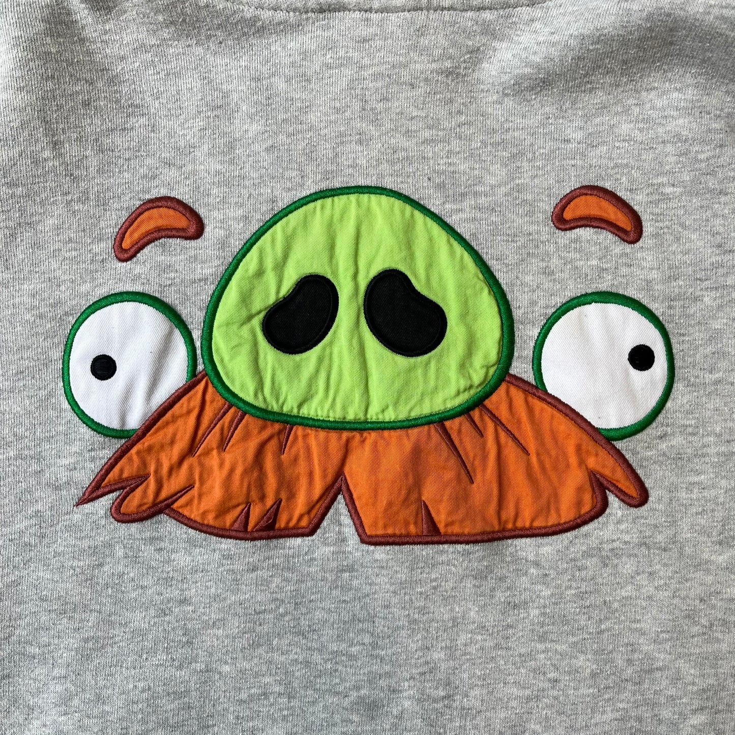 Angry Birds Three Star 2012 Foreman Pig Gray Hoodie features a grey hoodie design with a 3D-style front graphic of Foreman Pig, showing his recognizable eyes, nose, and mustache details. The back features a grey circular "Three Star" Angry Birds graphic, while the inside of the hood is finished with an orange lining.