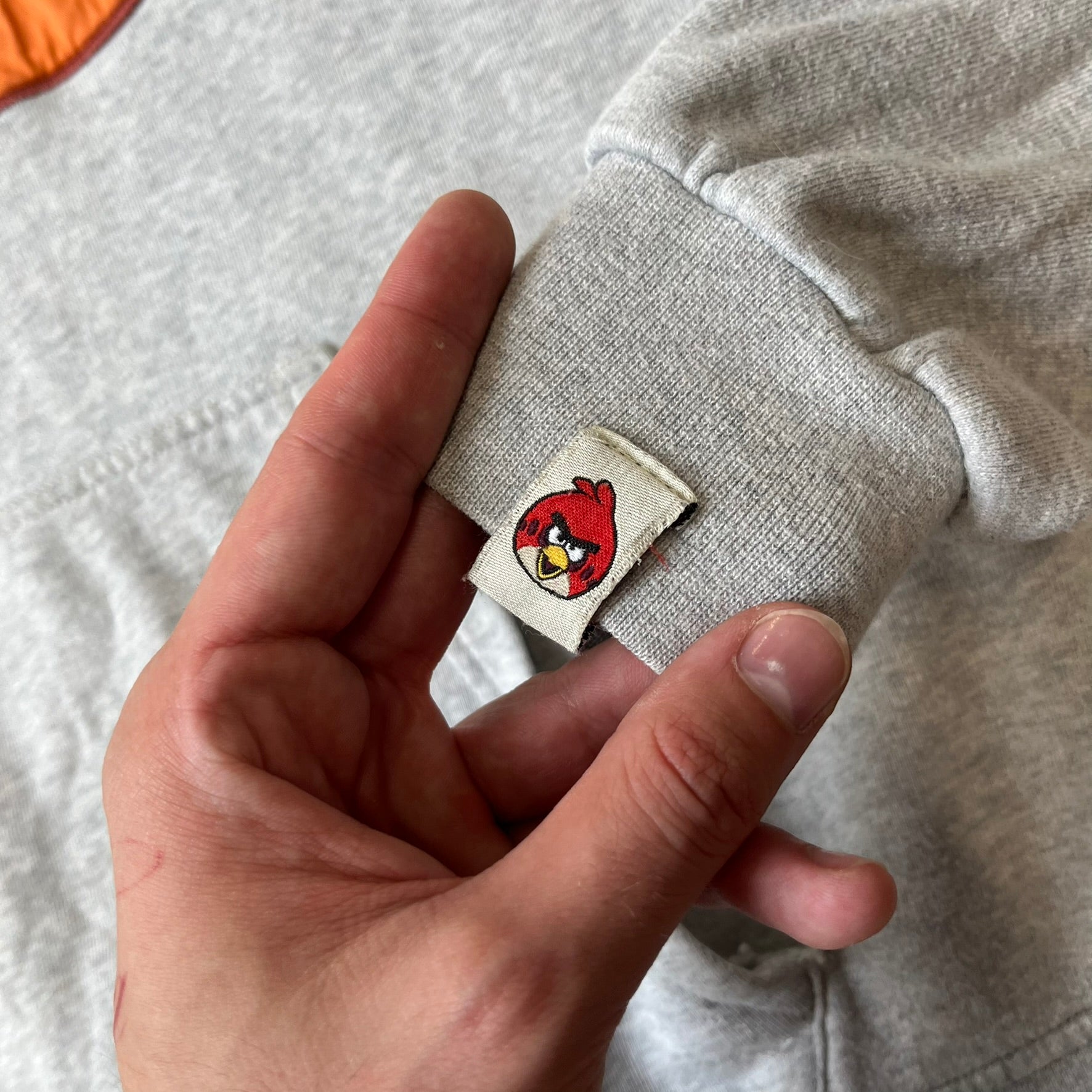 Angry Birds Three Star 2012 Foreman Pig Gray Hoodie features a grey hoodie design with a 3D-style front graphic of Foreman Pig, showing his recognizable eyes, nose, and mustache details. The back features a grey circular "Three Star" Angry Birds graphic, while the inside of the hood is finished with an orange lining.
