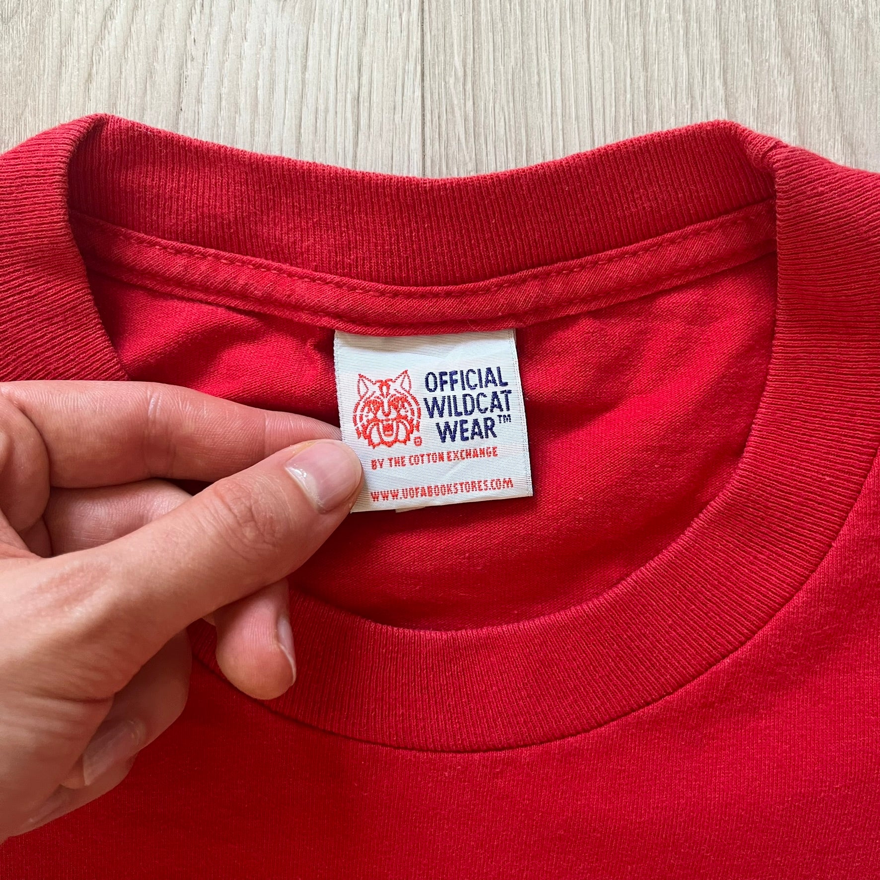 Red shirt with a visible label held by a hand on a light wooden surface