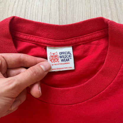 Red shirt with a visible label held by a hand on a light wooden surface