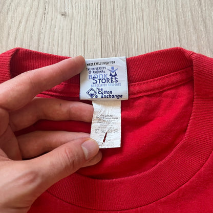 Red shirt with a tag held by a hand on a wooden surface
