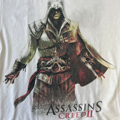 Assassin's Creed 2 Promo 2010 White Tee features a white 100% cotton construction with a large colorful graphic of Ezio Auditore da Firenze on the front. The Assassin's Creed 2 logo appears underneath the character, finished with a licensed neck tag.
