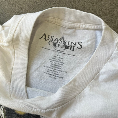 Assassin's Creed 2 Promo 2010 White Tee features a white 100% cotton construction with a large colorful graphic of Ezio Auditore da Firenze on the front. The Assassin's Creed 2 logo appears underneath the character, finished with a licensed neck tag.
