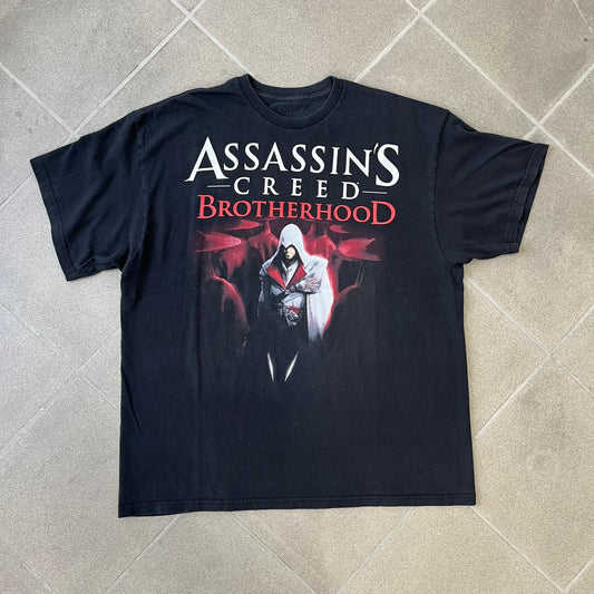Assassin's Creed Brotherhood 2010 Black Promo Tee features a black construction with the Assassin's Creed Brotherhood cover printed on the front, showing Ezio Auditore with the large white and red text above him. Finished with a washed-off licensed neck tag