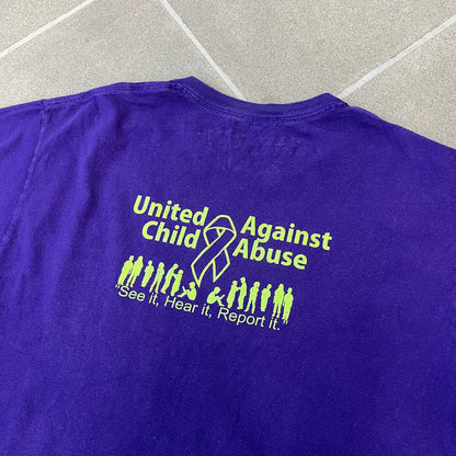 Asspizza 2024 Halloween Stars Purple Tee is a purple T-shirt featuring an all-over star pattern with orange and black stars outlined in green. Each star has a smiling face graphic in the center. The shirt includes a Babbitt 2024 neck tag and is printed on a Children’s Aid blank.
