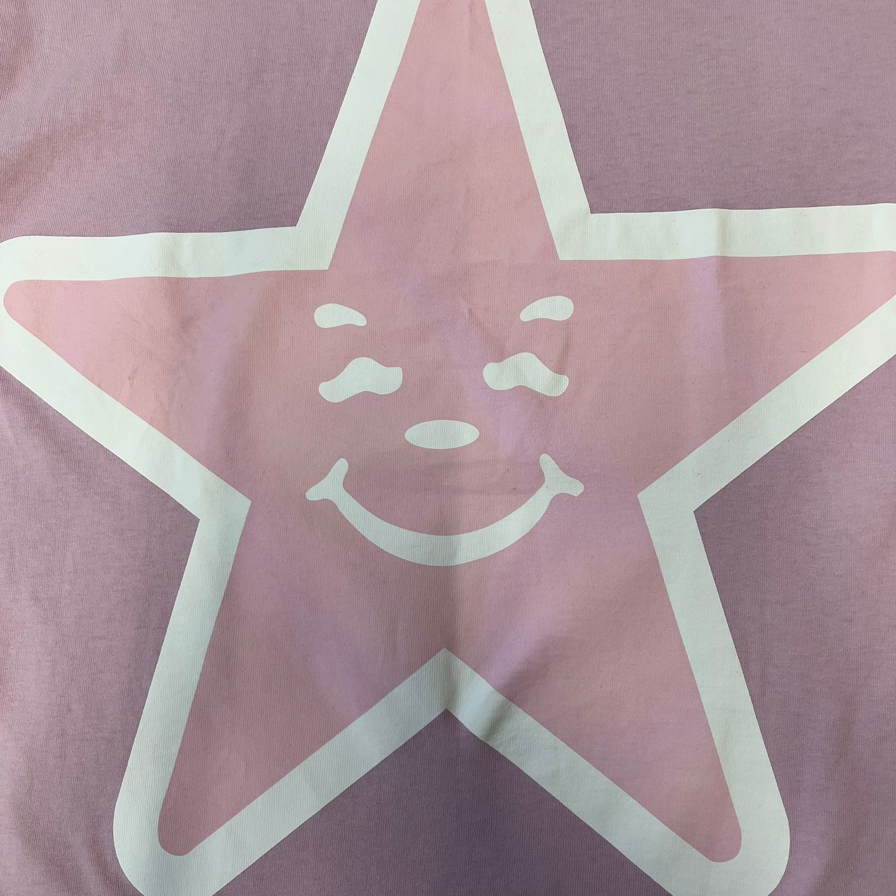 Asspizza 2025 Pink Star Tee is a dark pink T-shirt featuring a large light pink star graphic on the front. The star has a white outline and a white Happy Asspizza face design in the center. The shirt includes a red scribbled 2025 neck tag.
